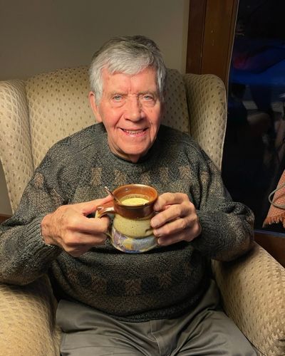Ron Thompson sits in a chair holding a mug