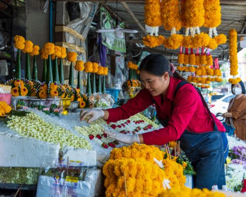 A woman at a market in Thailand arranges flowers for offerings, which people offer at Buddhist temples. 