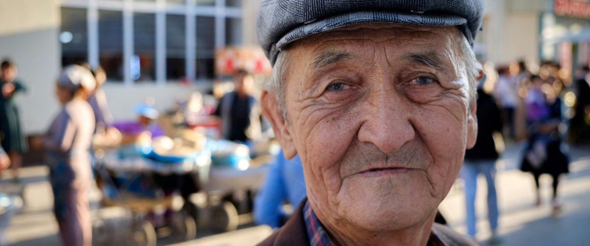 A Karakalpak man looks into the camera with people blurred in the background.